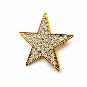 Puede incluir: Un broche de estrella de color dorado con diamantes de imitación transparentes.