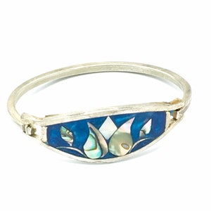 May include: A silver bangle bracelet with a blue enamel inlay featuring a floral design made of iridescent mother of pearl.