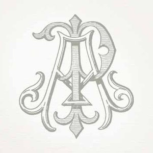 May include: A monogram design featuring the letters "A" and "R" intertwined in a decorative, stylized font. The letters are surrounded by ornate flourishes and scrolls.
