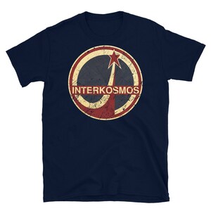 Könnte beinhalten: Ein marineblaues T-Shirt mit einem abgenutzten, rot-weiß-blauen Kreislogo, das ein stilisiertes Raumschiff und den Text "INTERKOSMOS" zeigt.