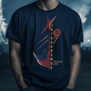 Puede incluir: Camiseta azul marino con un diseño gráfico retro que dice "Interkosmos Sputnik 1957". El diseño incluye una estrella roja, un cometa estilizado y una forma de ancla azul y roja. La camiseta tiene cuello redondo y mangas cortas.