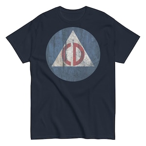 Könnte beinhalten: Marineblaues T-Shirt mit einem Used-Look-Design. Das Design umfasst einen hellblauen Kreis, ein weißes Dreieck und das rote Symbol "CD". Das Shirt besteht aus weichem Material und hat kurze Ärmel.