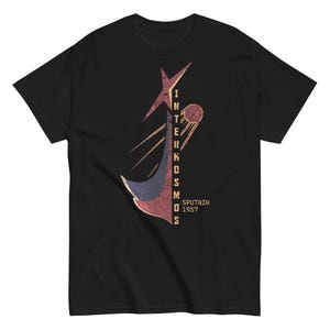 Puede incluir: Camiseta negra con un diseño gráfico retro. El diseño incluye el texto "INTERKOSMOS" y "SPUTNIK 1957", junto con una estrella, una forma curva y una ilustración de satélite.