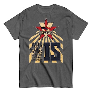 Puede incluir: Camiseta gris oscuro con un diseño gráfico. El diseño presenta una estrella roja con la palabra "INGSOC" y la frase "WAR IS PEACE FREEDOM IS SLAVERY IGNORANCE IS STRENGTH" en una fuente desgastada.