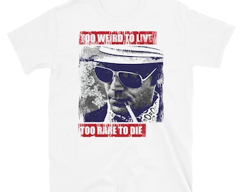 May include: White t-shirt with a distressed graphic of a man wearing sunglasses and a hat. The text "Too Weird To Live Too Rare To Die" is printed in red on the shirt.