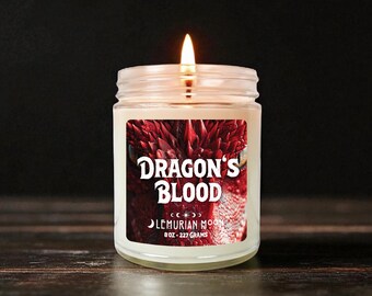 Può includere: Una candela accesa in un barattolo di vetro con un'etichetta che recita "Dragon's Blood" in lettere bianche. L'etichetta presenta un primo piano del volto di un drago rosso. La candela è di 227 grammi.