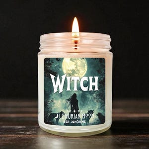 May include: A lit glass jar candle with a label that reads "Witch" over an illustration of a woman, wolves, and a full moon. The candle is labeled "Lemurian Moon" and weighs 8 oz (227 grams).