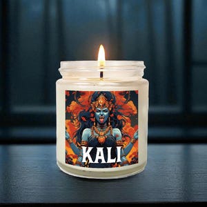 Puede incluir: Una vela encendida en un frasco de vidrio con una etiqueta que presenta una ilustración de la diosa hindú Kali. La obra de arte representa a Kali con piel azul, una corona y múltiples brazos. La palabra "KALI" está impresa en blanco.