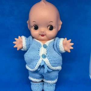 Pu&ograve; includere: Una bambola di porcellana vintage che indossa un completo di maglia blu con rifiniture bianche. La bambola ha occhi grandi e un sorriso dipinto.