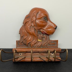 Op de afbeelding: Een houten sleutelhanger met een gegraveerd bruin hondenhoofd en vier haken. De hond heeft een gouden halsband en een bruin-wit geschilderd gezicht.