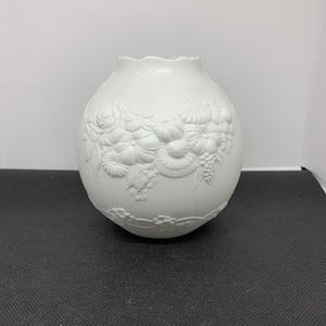 Może przedstawiać: Biały ceramiczny wazon z wypukłym wzorem kwiatowym. Wazon jest okrągły i ma falisty brzeg.