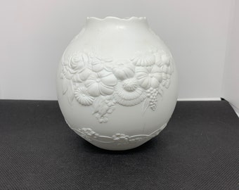 May include: White ceramic vase with a raised floral design. The vase is round and has a scalloped rim.