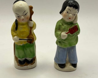 Könnte beinhalten: Zwei kleine Keramikfiguren von Menschen in traditioneller chinesischer Kleidung. Die Figur links hält ein Musikinstrument und trägt ein gelbes Hemd und eine grüne Hose. Die Figur rechts hält einen Fächer und trägt ein grünes Hemd und eine blaue Hose.