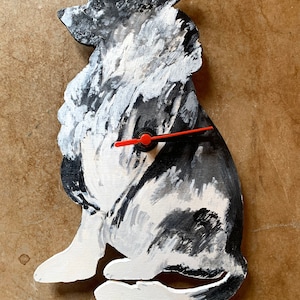 Könnte beinhalten: Eine schwarz-weiß bemalte Holzuhr in Form eines Hundes. Die Uhr hat rote Zeiger und einen schwarzen Knopf in der Mitte.