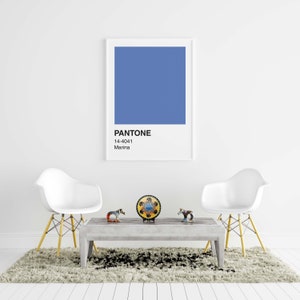 May include: A framed print featuring a Pantone color swatch in Marina blue, with the color code 14-4041. The print hangs above a gray coffee table with decorative figurines and two white chairs with yellow legs. The room has a neutral color palette.