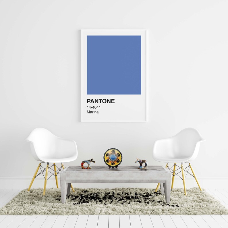 May include: A framed print featuring a Pantone color swatch in Marina blue, with the color code 14-4041. The print hangs above a gray coffee table with decorative figurines and two white chairs with yellow legs. The room has a neutral color palette.