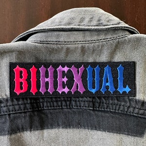 May include: A gray denim jacket with a black patch that says "Bisexual" in rainbow colors.