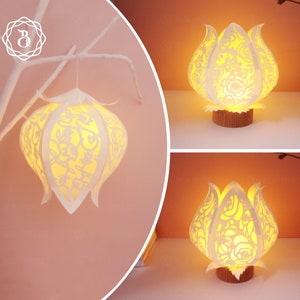 Puede incluir: Lámpara de papel blanco con forma de flor con intrincados recortes. La lámpara está encendida y proyecta un cálido resplandor.