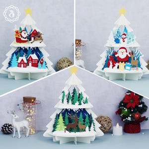 May include: White paper Christmas tree decorations with layered cutouts of Santa Claus, reindeer, houses, and trees. Each tree has a yellow star on top. Festive holiday decor.