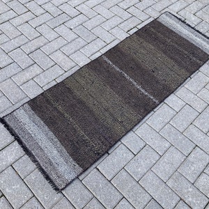 以下が含まれることがあります： フリンジの縁取りのある黒とグレーのストライプの敷物。敷物は織物で作られており、表面にテクスチャがあります。