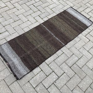 Op de afbeelding: Een bruin en wit gestreept tapijt met een geweven textuur. Het tapijt heeft een lange, rechthoekige vorm en is gemaakt van natuurlijke vezels.