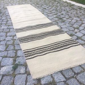 May include: A white and brown patterned runner rug with a fringe edge. The rug has a geometric design with brown stripes and a white background.