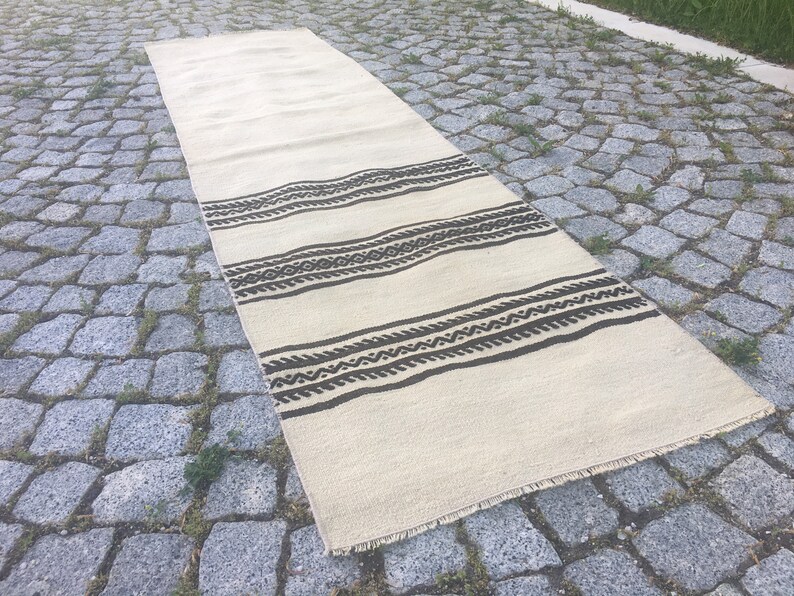 May include: A white and brown patterned runner rug with a fringe edge. The rug has a geometric design with brown stripes and a white background.