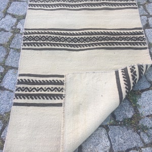 May include: A white and brown woven rug with geometric patterns. The rug is folded in half and lying on a stone surface.