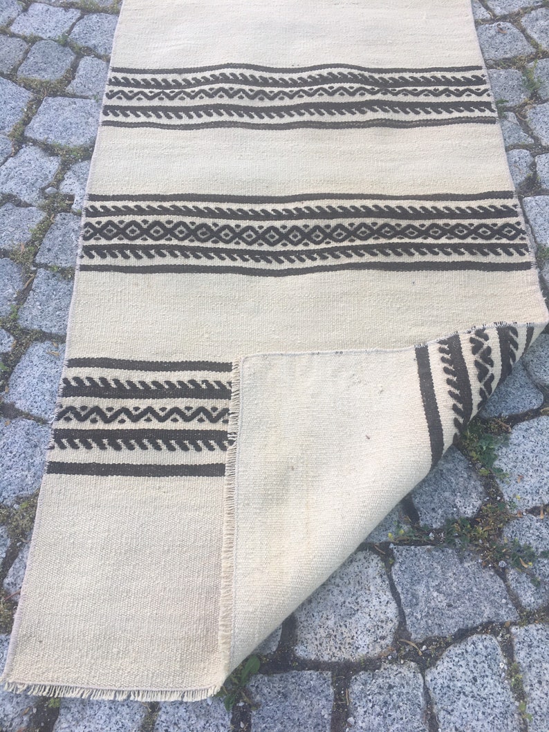 May include: A white and brown woven rug with geometric patterns. The rug is folded in half and lying on a stone surface.