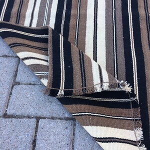 May include: A striped rug with black, brown, and white stripes. The rug is folded in half and the edges are frayed.