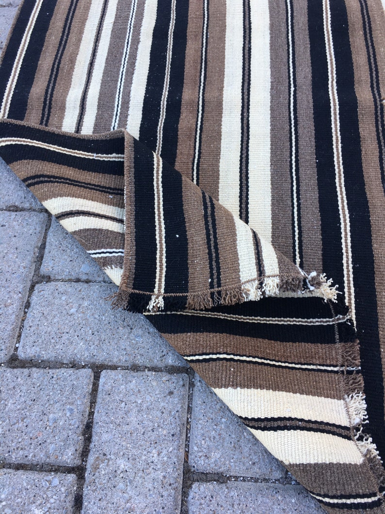 May include: A striped rug with black, brown, and white stripes. The rug is folded in half and the edges are frayed.