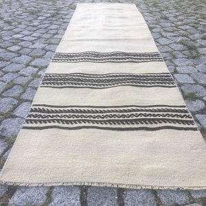 May include: A white and brown striped rug with a geometric pattern. The rug has a fringe border and is lying on a stone surface.