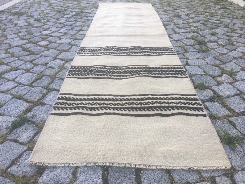 May include: A white and brown striped rug with a geometric pattern. The rug has a fringe border and is lying on a stone surface.