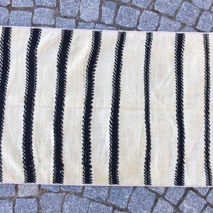 K&ouml;nnte beinhalten: Ein wei&szlig;er und schwarzer gestreifter Teppich mit einem subtilen, geschwungenen Muster in den schwarzen Streifen. Der Teppich hat einen Fransenrand.