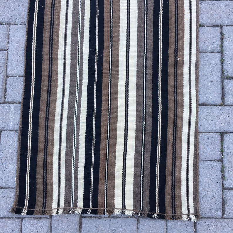 May include: A striped rug with black, brown, and white stripes. The rug has a fringe on the bottom edge.