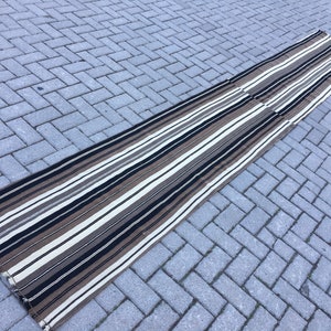 May include: A long, striped rug with black, white, and brown stripes. The rug is made of a woven material and has a fringed edge.