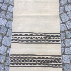 May include: A white runner rug with black geometric patterns. The rug has two bands of black geometric designs.