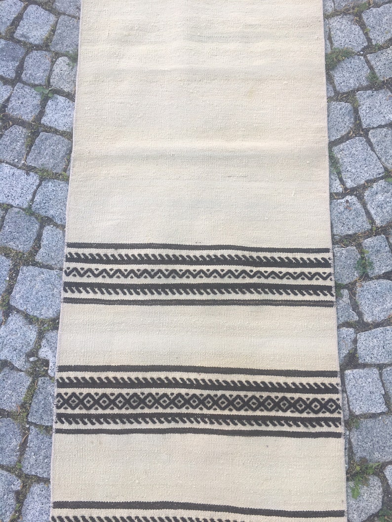 May include: A white runner rug with black geometric patterns. The rug has two bands of black geometric designs.