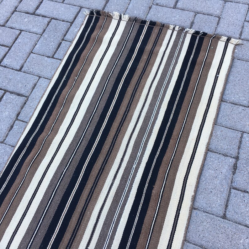 May include: A striped rug with black, brown, and white stripes. The rug has a fringe on the top and bottom.