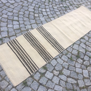 May include: A long, off-white runner rug with a black and white geometric pattern. The rug has a simple, modern design and would be a great addition to any home.