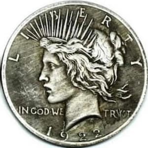 May include: A silver coin with a profile of a woman wearing a crown of rays. The coin has the text "LIBERTY", "IN GOD WE TRUST", and the year "1922". The coin is a Peace Dollar.