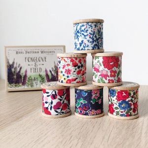 May include: Six wooden spools with floral patterned fabric wrapped around them. The spools are arranged in a pyramid shape. The fabric patterns are in shades of blue, red, and white.
