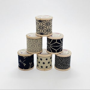 Może przedstawiać: Sześć szpulek nici z różnymi czarno-białymi wzorami. Szpulki są drewniane i mają etykietę z napisem "Foxglove & Field".