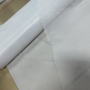 May include: Two white fabric swatches, one rolled up and the other lying flat. The fabric has a smooth, silky texture.