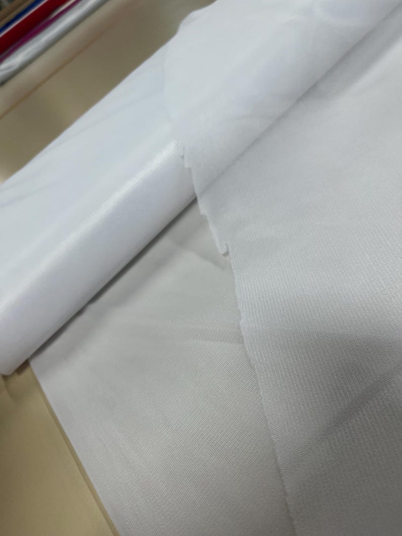 May include: Two white fabric swatches, one rolled up and the other lying flat. The fabric has a smooth, silky texture.