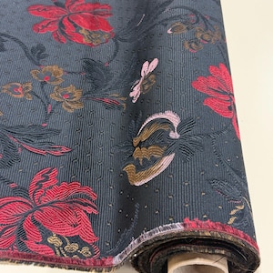 May include: A roll of dark blue fabric with a floral pattern. The design features large red flowers, along with smaller gold and pink floral accents. The fabric has a textured, vertical striped background.
