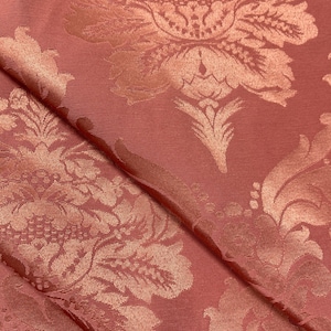 May include: A close-up of a pink fabric with a raised, embossed floral pattern. The fabric has a subtle sheen and a soft texture.