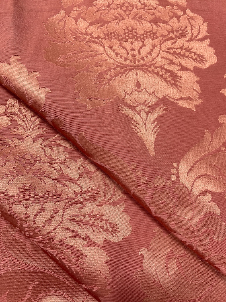 May include: A close-up of a pink fabric with a raised, embossed floral pattern. The fabric has a subtle sheen and a soft texture.