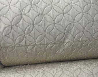 May include: A roll of off-white fabric with a quilted geometric pattern. The design features overlapping circles stitched into the material. The fabric appears soft and has a subtle sheen, suitable for various sewing projects.
