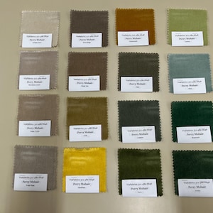 May include: A collection of sixteen fabric swatches in various colors, including beige, brown, green, and yellow. Each square has a label with the text "Perry Mohair". The swatches are arranged in four rows and four columns on a light beige surface.
